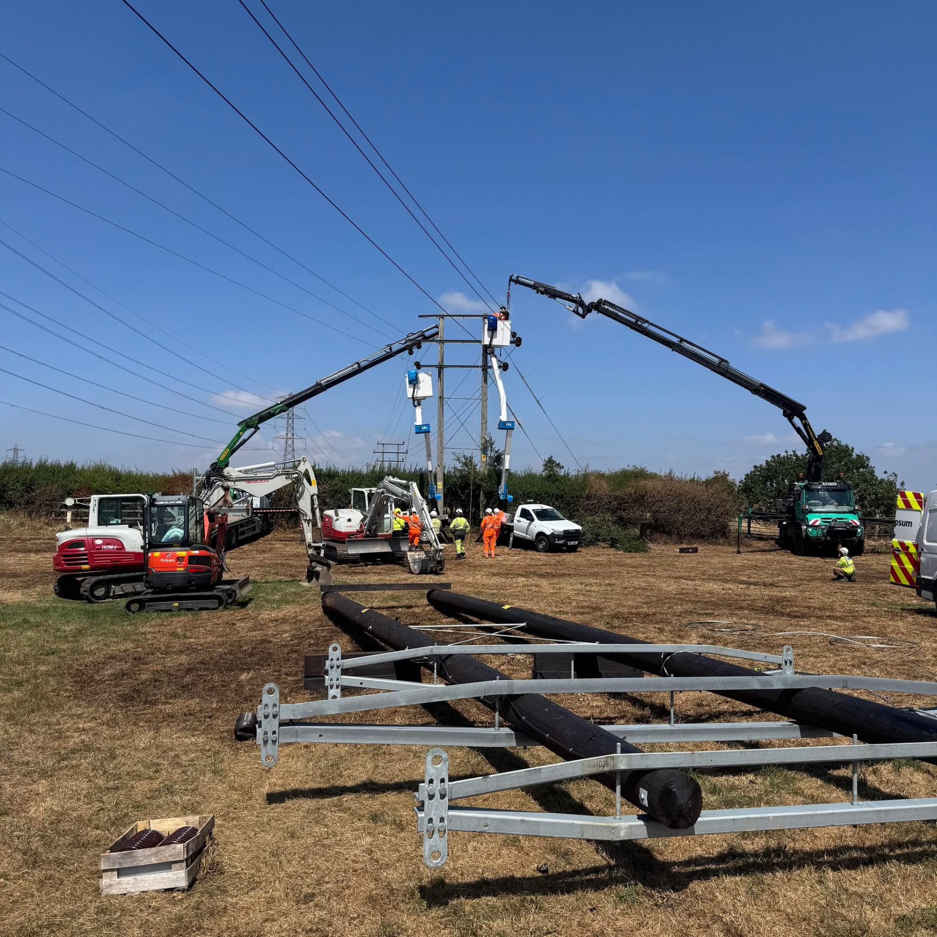 UK OHL crew working on an H-pole from two MEWPs, with an excavator on site