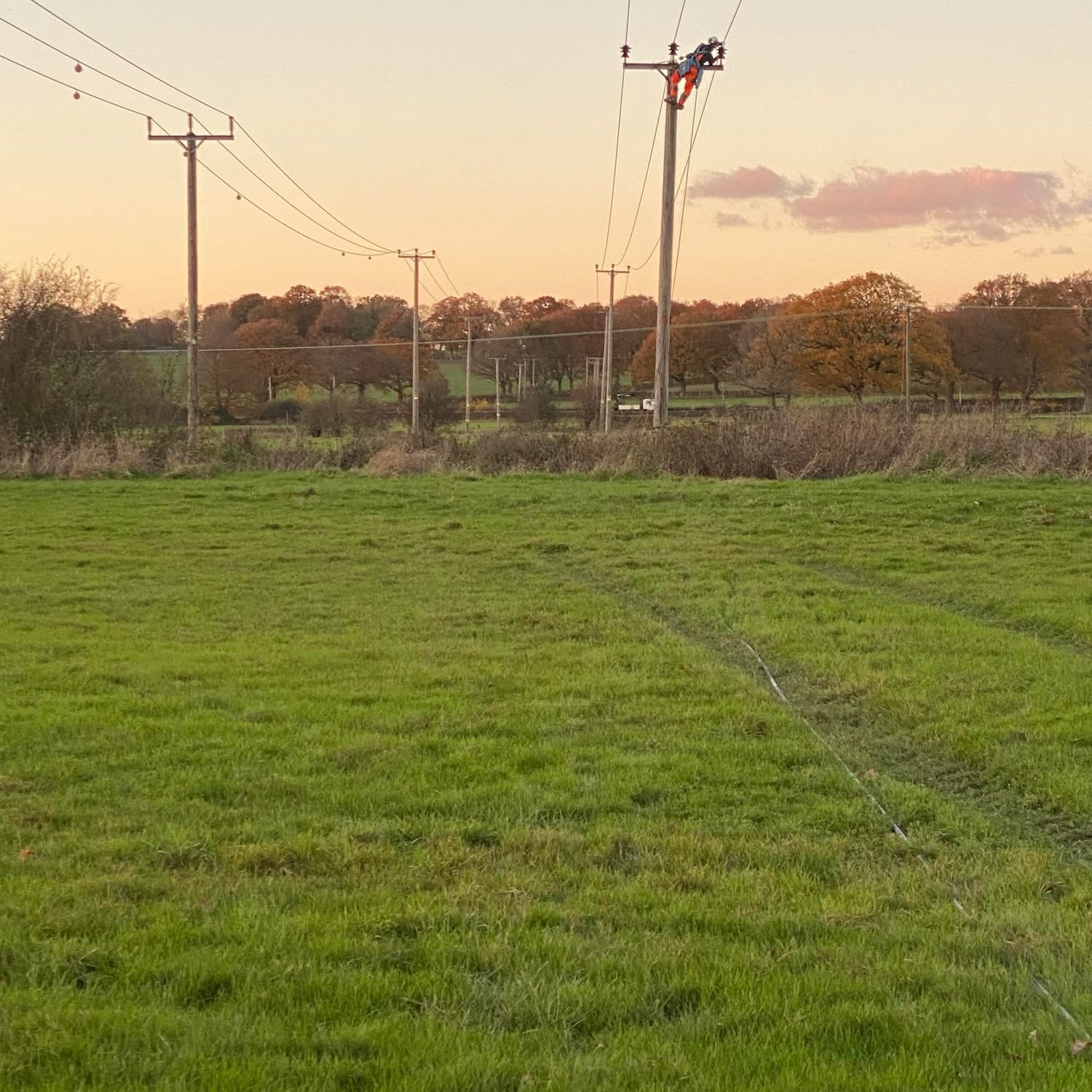 Linesman working at the top of a pole at sunset